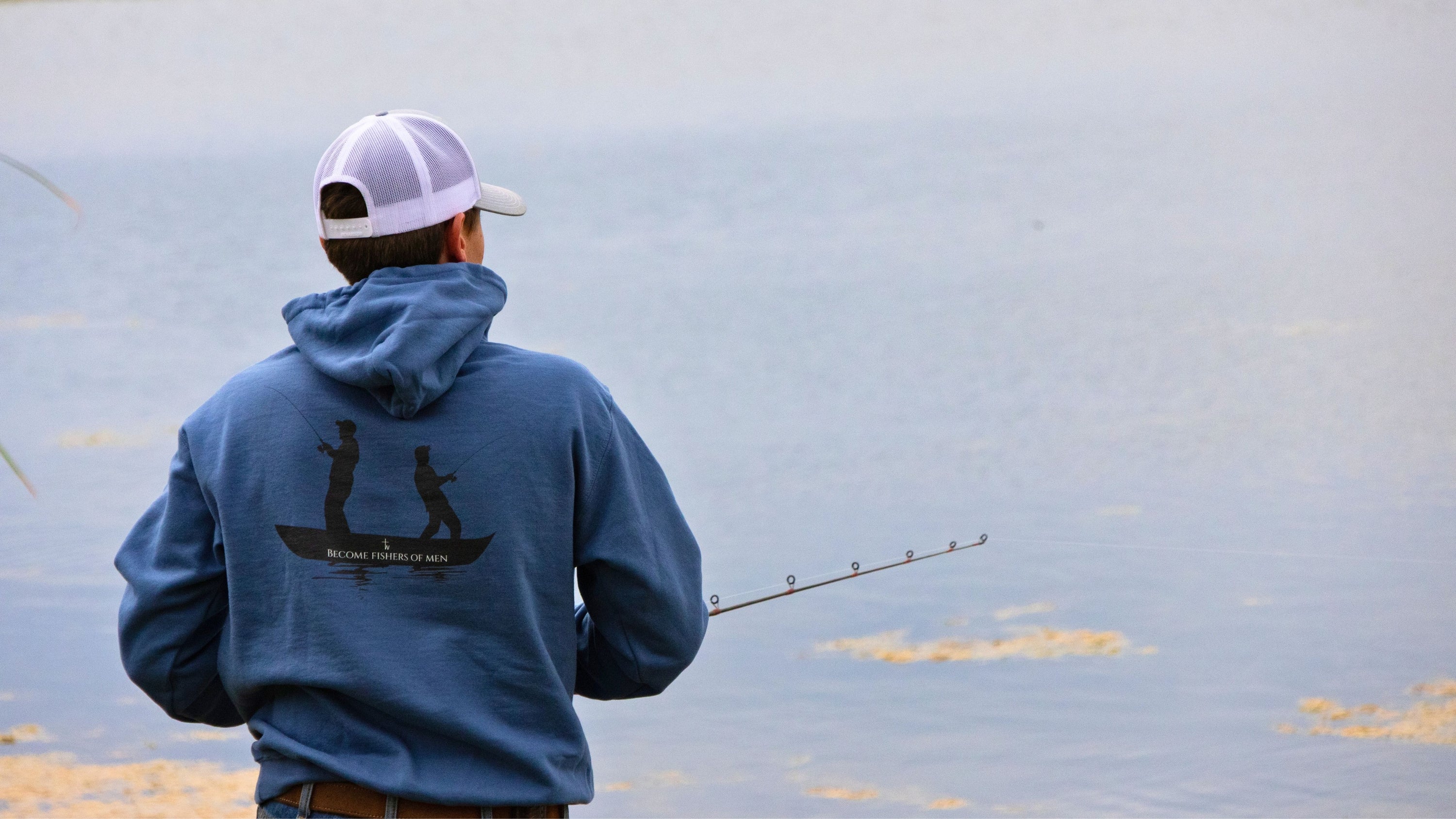 Man fishing on a lake wearing a blue hoodie with a logo.